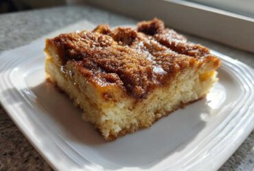 A square slice of baked french toast with a rich, caramelized cinnamon sugar topping on a white plate.