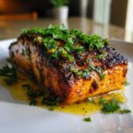 A close-up of a perfectly cooked piece of blackened salmon topped with fresh parsley and resting in butter sauce.