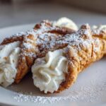 Close-up of two freshly filled cannoli, dusted with powdered sugar, ready to eat.