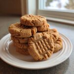 A tempting stack of freshly baked peanut butter cookies showing classic crisscross fork marks on a white plate.