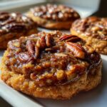A close-up, appetizing shot of several pecan pie cookies topped with a sticky, glossy glaze and whole pecan halves.
