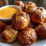A plate piled high with freshly baked pretzel bites sprinkled with coarse salt, next to a small bowl of bright orange cheese sauce.