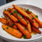 Close-up of glossy, glazed roasted carrots topped with fresh chopped parsley in a white bowl.