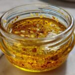 Close-up of a vibrant, golden homemade salad dressing with visible spices and seeds inside a small glass jar.