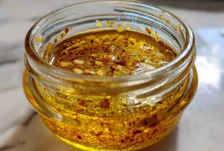 Close-up of a vibrant, golden homemade salad dressing with visible spices and seeds inside a small glass jar.