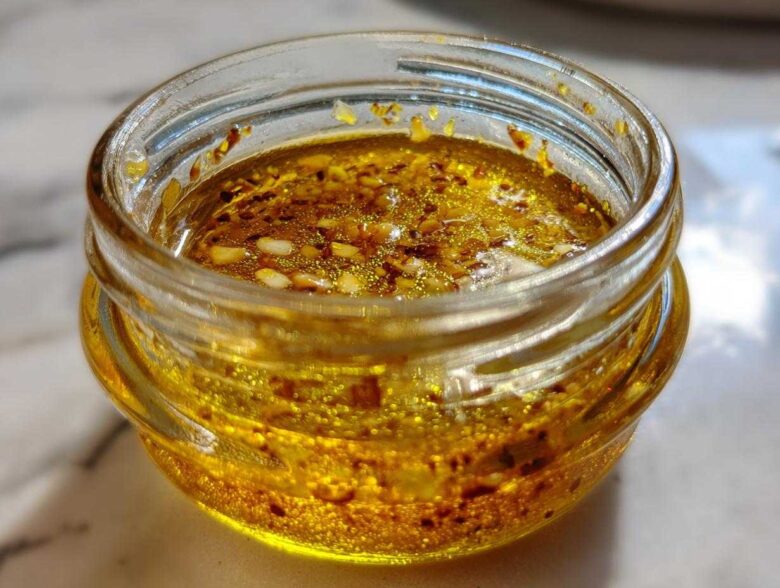 Close-up of a vibrant, golden homemade salad dressing with visible spices and seeds inside a small glass jar.