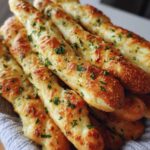 A close-up stack of golden, soft breadsticks brushed with garlic butter and sprinkled with fresh parsley.