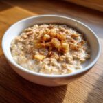 A white bowl filled with creamy apple cinnamon oatmeal, topped with diced apples and cinnamon.