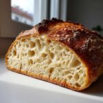 Close-up of artisan bread cut in half, showcasing a light, airy crumb structure and dark, crispy crust.