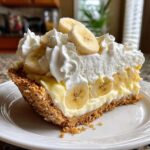 A rich slice of banana cream pie recipe featuring a graham cracker crust, thick custard, and whipped cream topped with banana slices.