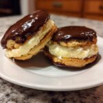 Two delicious boston cream pie cookies filled with vanilla cream and topped with shiny chocolate glaze.