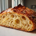 Close-up of a freshly baked bread loaf cut in half showing an open, airy crumb structure and dark, blistered crust.