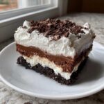 A rich slice of brownie refrigerator cake showing multiple layers of chocolate and cream, topped with whipped cream and chocolate shavings.