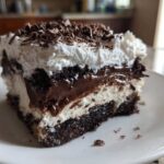 Close-up of a rich slice of brownie refrigerator cake showing layers of dark chocolate, white cream, and chocolate shavings.