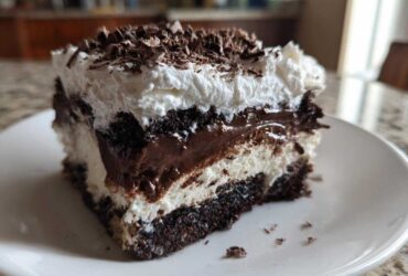 Close-up of a rich slice of brownie refrigerator cake showing layers of dark chocolate, white cream, and chocolate shavings.