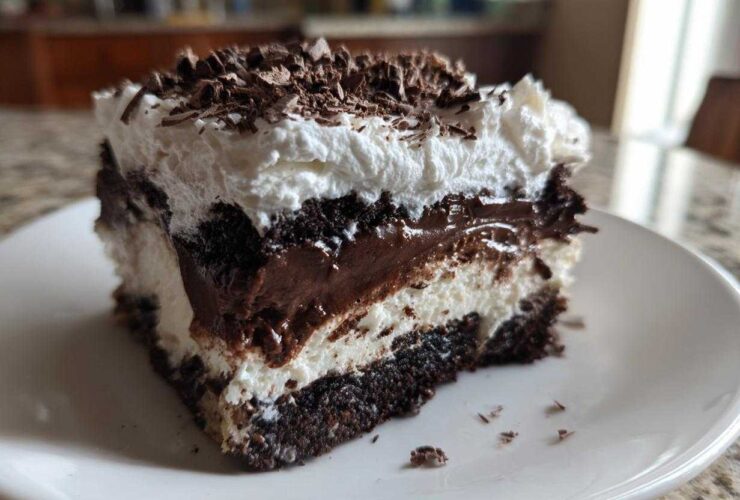 Close-up of a rich slice of brownie refrigerator cake showing layers of dark chocolate, white cream, and chocolate shavings.