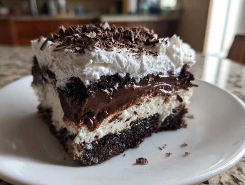 Close-up of a rich slice of brownie refrigerator cake showing layers of dark chocolate, white cream, and chocolate shavings.