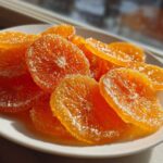 Close-up of glistening, bright orange candied orange slices dusted with sparkling sugar.