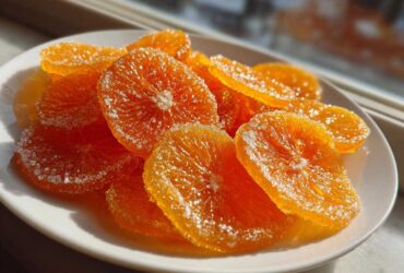 Close-up of glistening, bright orange candied orange slices dusted with sparkling sugar.