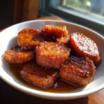 Thick slices of candied sweet potatoes glistening with rich brown syrup in a white bowl.