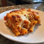A close-up of a hearty slice of cheesy pasta bake featuring rigatoni pasta, rich sauce, and melted, browned mozzarella cheese.