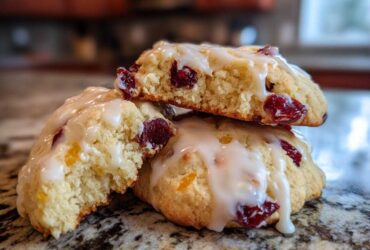 Close-up of chewy cranberry orange cookies stacked, drizzled with white citrus glaze.