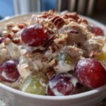 A close-up of creamy chicken salad chick grape salad topped generously with red and green grapes and chopped pecans.