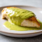 A perfectly cooked chicken breast topped generously with vibrant green cilantro lime sauce on a white plate.