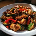Close-up of glossy chicken zucchini stir fry pieces coated in sauce and sprinkled with sesame seeds.