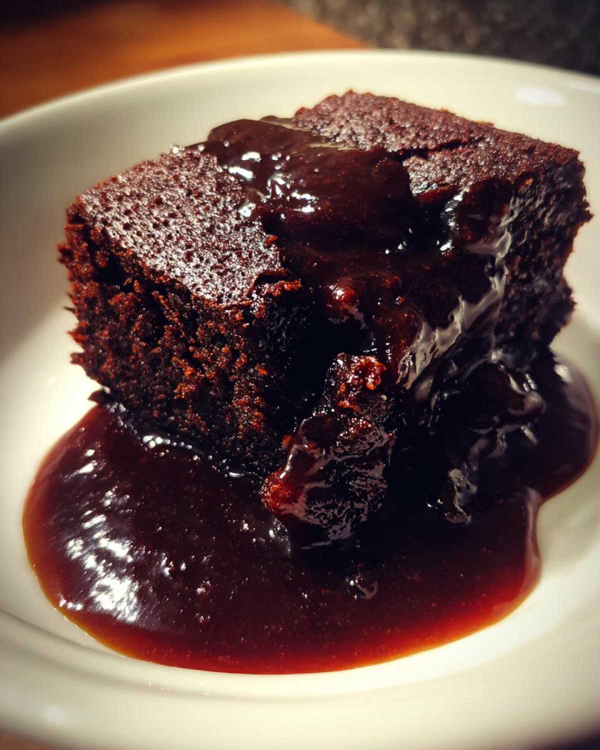 Close-up of a moist slice of chocolate pudding cake covered in rich, dark chocolate sauce.