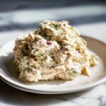 A mound of creamy cottage cheese chicken salad mixed with fresh dill and red onion pieces, served on a white plate.