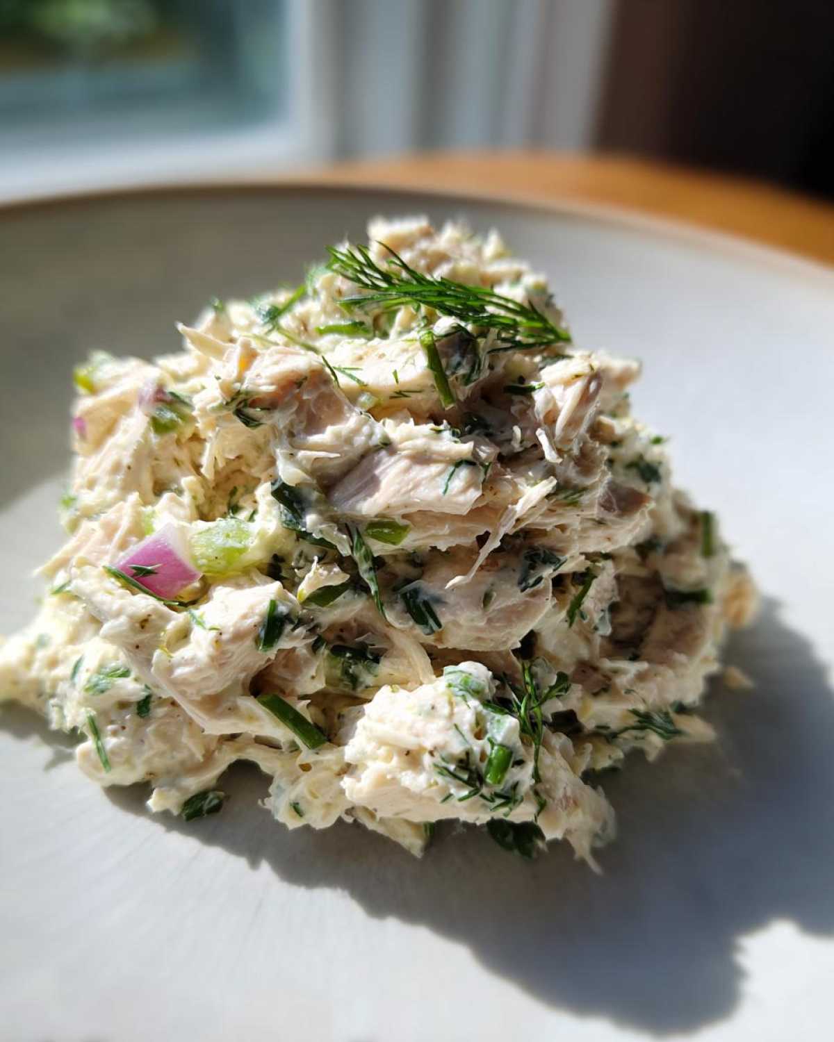 A mound of creamy cottage cheese chicken salad mixed with herbs and diced red onion, garnished with fresh dill.