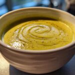 Close-up of a bowl of vibrant green, creamy celery soup, drizzled with a swirl of olive oil.