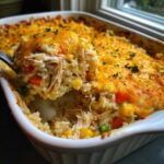 A spoonful of creamy chicken and rice casserole topped with melted cheddar cheese being lifted from a white baking dish.