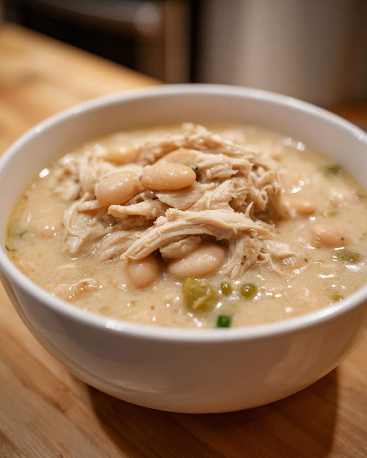 Close-up of a white bowl filled with creamy white chicken chili, topped with shredded chicken and white beans.
