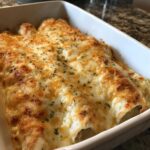 Close-up of freshly baked creamy chicken enchiladas covered in melted white and cheddar cheese and sprinkled with herbs.