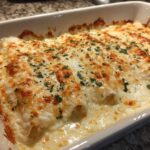 Close-up of baked creamy chicken enchiladas covered in melted, bubbly white cheese and garnished with parsley.