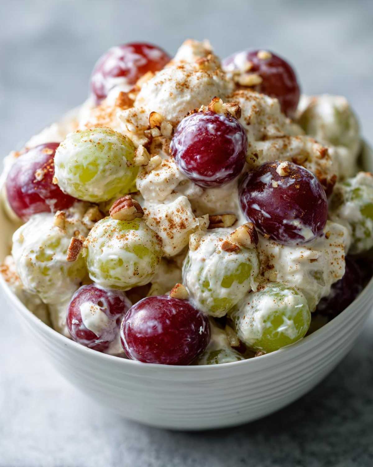 Close-up of creamy chicken salad chick grape salad featuring red and green grapes coated in dressing, topped with pecans and cinnamon.