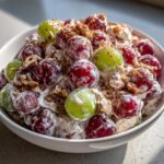 A close-up of creamy chicken salad chick grape salad, featuring red and green grapes coated in dressing and topped with pecans and cinnamon.