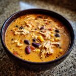 Close-up of a bowl of creamy chicken taco soup filled with shredded chicken, black beans, and corn.