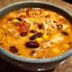 Close-up of a bowl of creamy chicken taco soup with shredded chicken, black beans, corn, and tomatoes.
