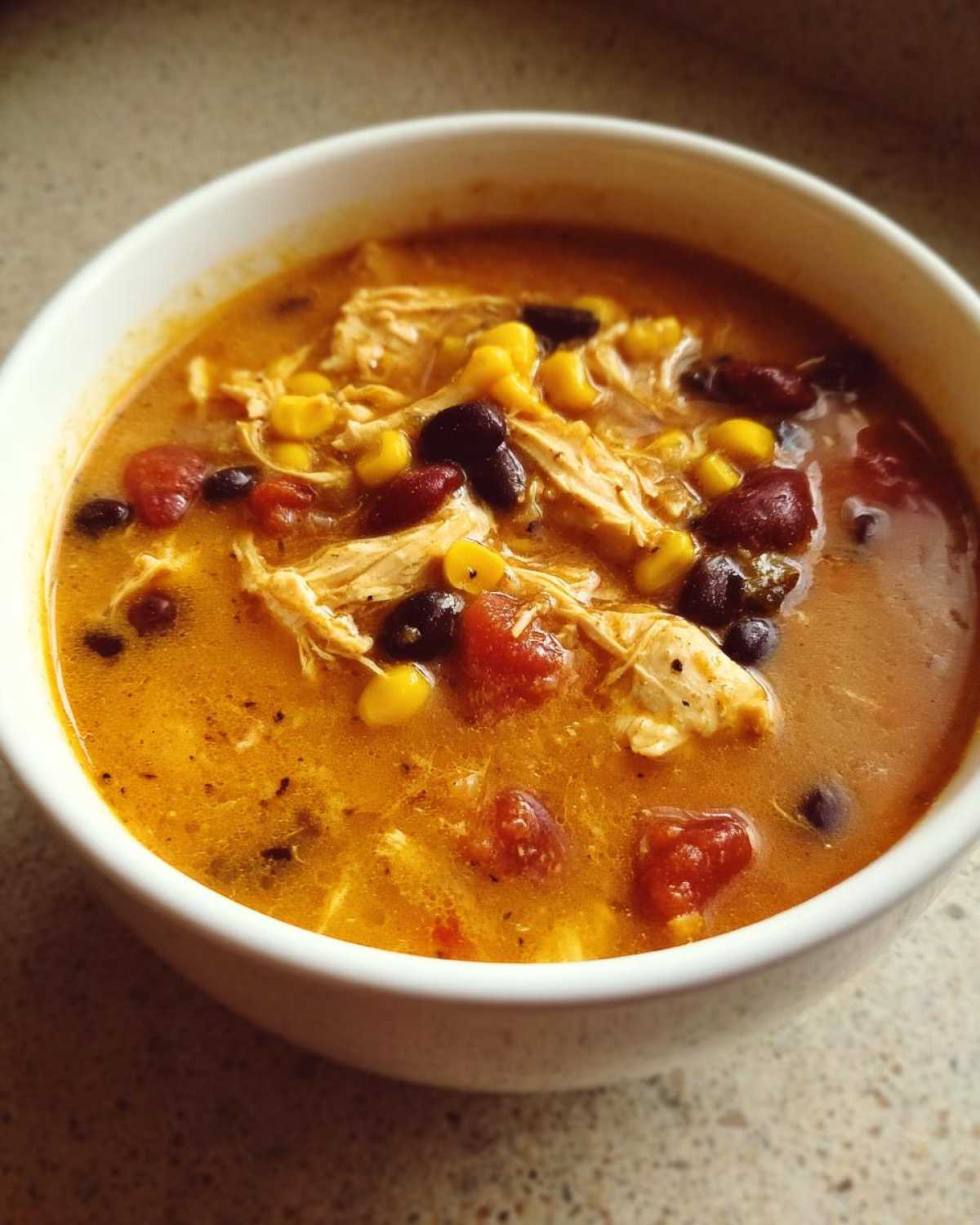 Close-up of a bowl of creamy chicken taco soup filled with shredded chicken, corn, black beans, and tomatoes.