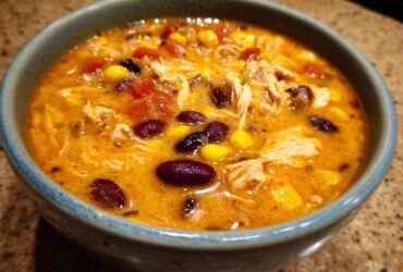 Close-up of a bowl of creamy chicken taco soup with shredded chicken, black beans, corn, and tomatoes.