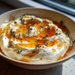 A close-up of a bowl filled with creamy ricotta dip drizzled generously with honey and garnished with fresh thyme sprigs.