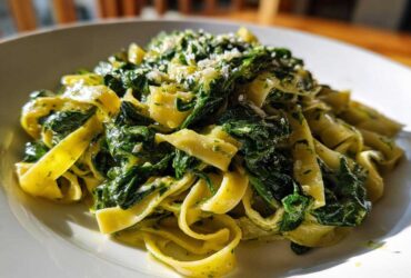 A close-up of creamy spinach pasta featuring fettuccine noodles coated in a light sauce and topped with grated Parmesan cheese.