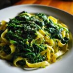 Close-up of creamy spinach pasta featuring fettuccine noodles generously topped with wilted spinach and grated cheese.