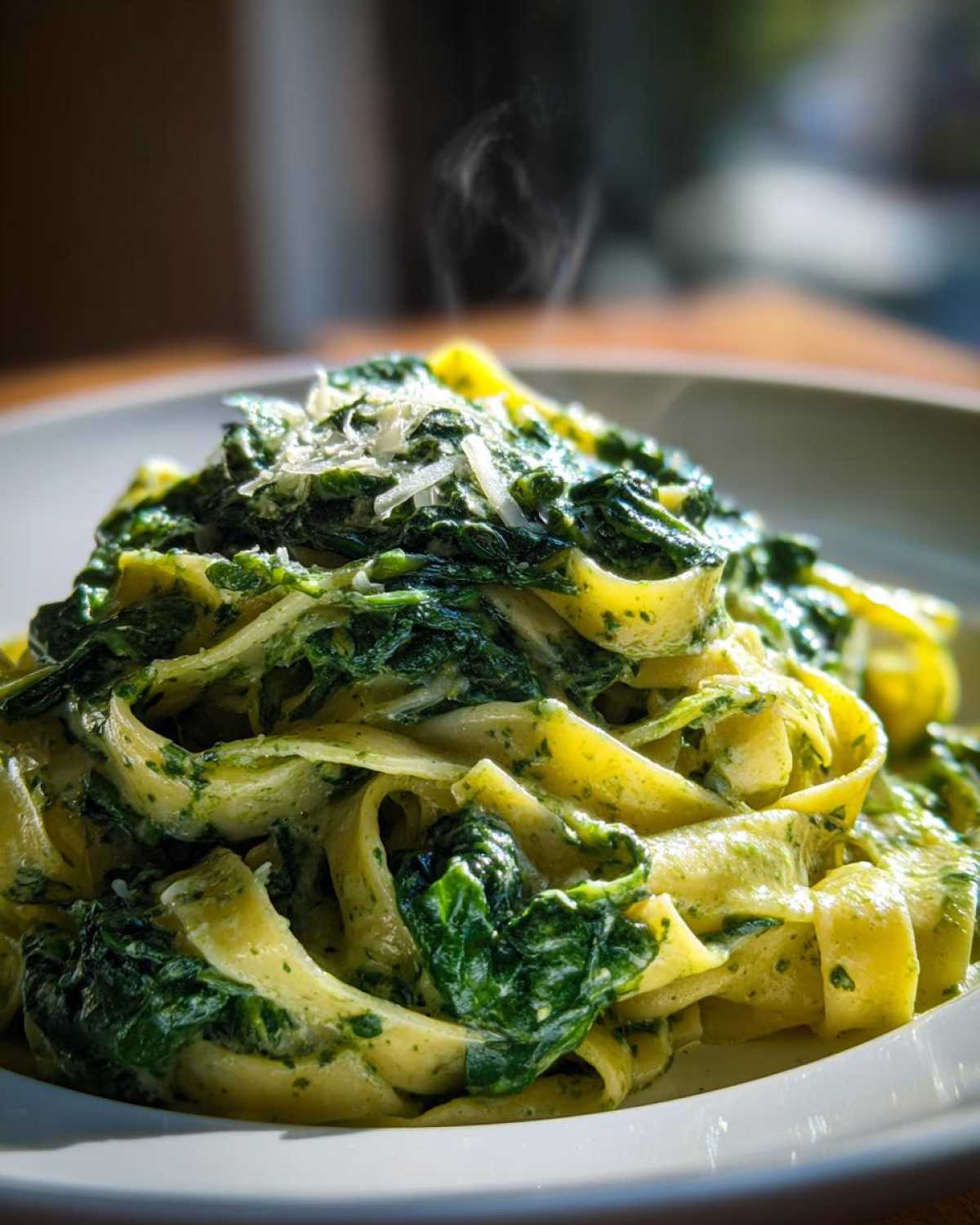 Close-up of steaming fettuccine tossed in a creamy sauce with wilted spinach, topped with grated Parmesan cheese, representing amazing spinach pasta.