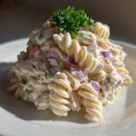 A mound of creamy tuna pasta salad made with rotini pasta, red onion, and topped with fresh parsley.