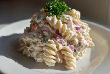 A mound of creamy tuna pasta salad made with rotini pasta, red onion, and topped with fresh parsley.
