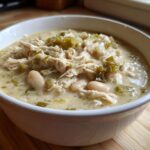 Close-up of a white bowl filled with creamy white chicken chili, featuring shredded chicken, white beans, and green chilies.